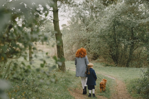 Madre e figlia che giocano con il cane. Famiglia nella sosta di autunno. Pet, animali domestici e concetto di stile di vita. Tempo d'autunno.