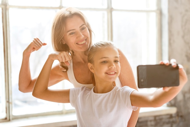 Madre e figlia che prendono selfie che flette i muscoli del braccio