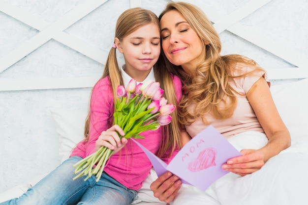 Madre e figlia che si siedono con i fiori e la cartolina d&#39;auguri