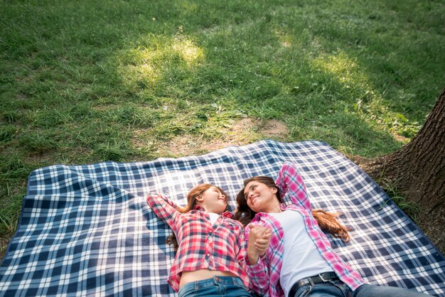 Madre e figlia che tengono la loro mano che si trova sulla coperta nel parco