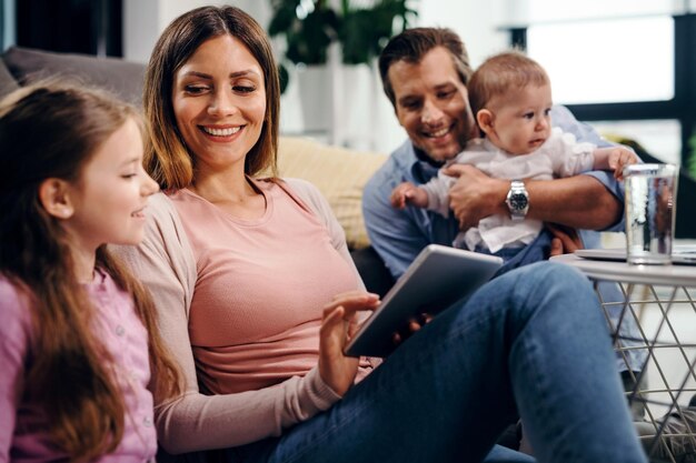 Madre e figlia felici che usano la tavoletta digitale mentre il padre tiene un bambino a casa