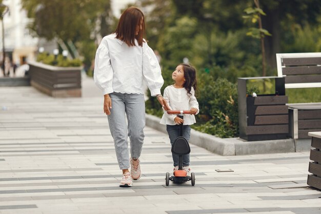 Madre e figlia sul motorino di scossa nel parco. I bambini imparano a pattinare sul roller. Bambina che pattina sulla soleggiata giornata estiva.