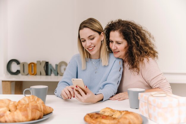 Madre e figlia utilizzando smartphone durante la colazione