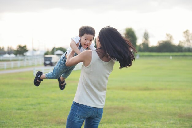 Madre e figlio che giocano nel parco all'ora del tramonto. gente che si diverte in campo. concetto di famiglia amichevole e di vacanza estiva. madre che lancia suo figlio in aria.