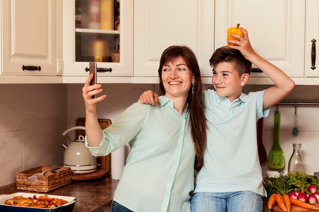 Madre e figlio che prendono selfie in cucina