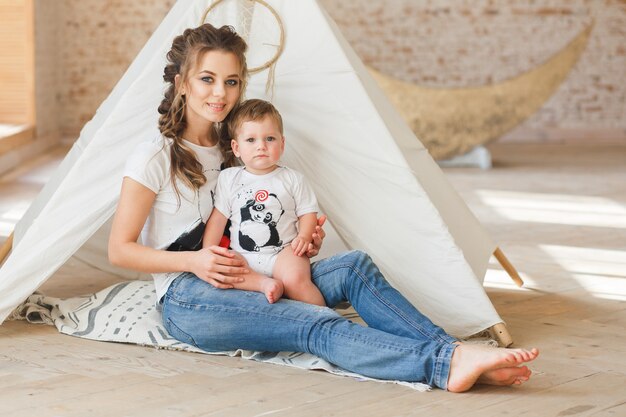 Madre e figlio che si siedono posando vicino alla tenda nel monolocale studio del sottotetto con il fondo del muro di mattoni