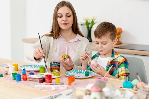 Madre e figlio dell'angolo alto concentrati per dipingere le uova