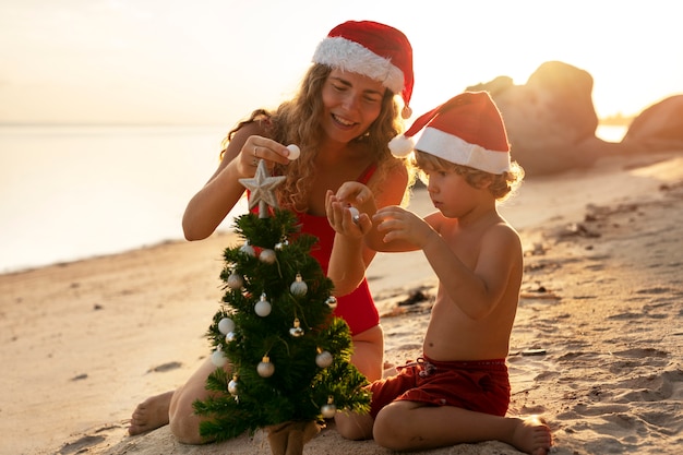 Madre e figlio sulla spiaggia con i cappelli di Babbo Natale