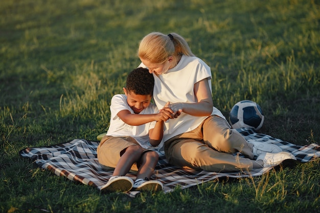 Madre europea e figlio africano. Famiglia in un parco estivo. Persone sedute sulla coperta.