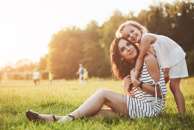 Madre felice e figlia che abbracciano in un parco al sole su un'estate luminosa di erbe.