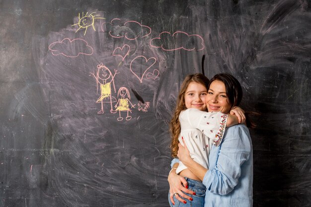 Madre felice e figlia che abbracciano vicino alla lavagna con disegno