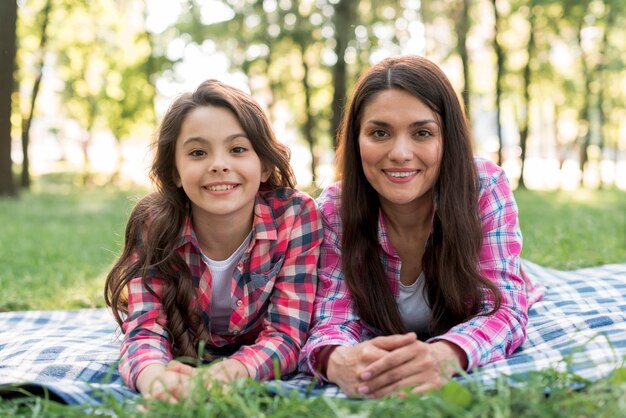 Madre felice e figlia che esaminano macchina fotografica che si trova sulla coperta sopra terra erbosa in parco