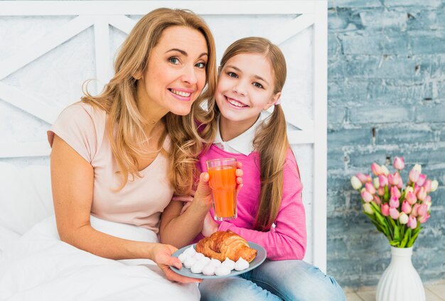 Madre felice e figlia che si siedono con il croissant sul letto