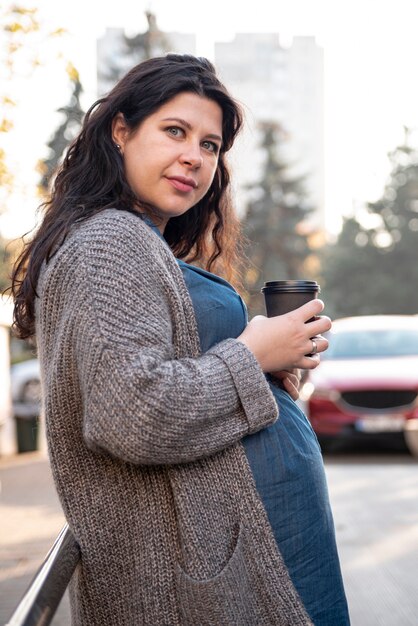 Madre futura del colpo medio con la tazza di caffè