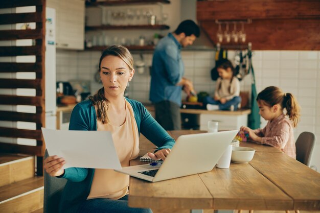 Madre lavoratrice che analizza i rapporti mentre utilizza il laptop a casa