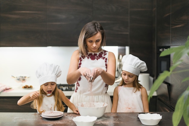 Madre mescolando la polvere di cacao per fare biscotti con le sue figlie in cucina