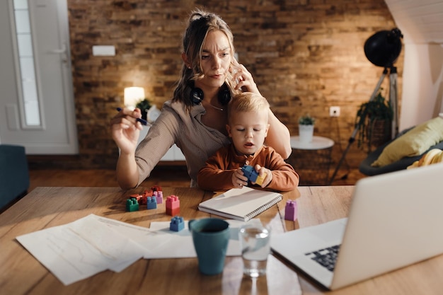 Madre multitasking che fa da babysitter al suo piccolo figlio mentre lavora da casa