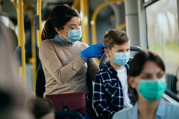 Madre premurosa che mette una maschera protettiva sul viso del figlio mentre si sposta in autobus