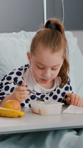 Madre seduta accanto alla figlia malata mentre mangia il pranzo in convalescenza dopo un intervento chirurgico