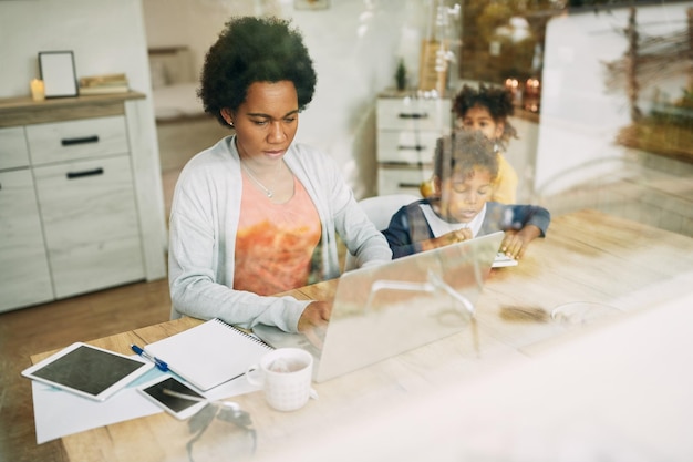 Madre single afroamericana con due bambini che lavorano al computer portatile a casa