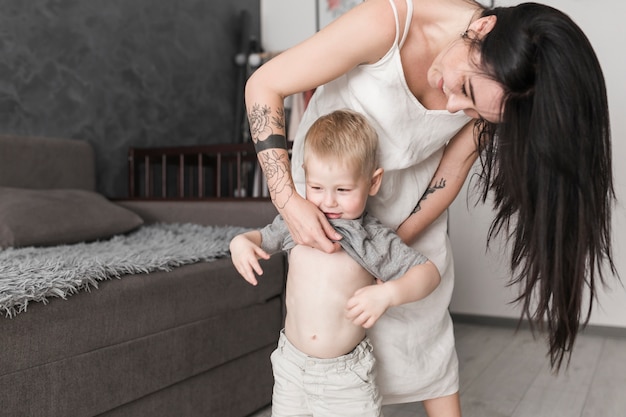 Madre sorridente con lunghi capelli neri che cambiano i vestiti di suo figlio