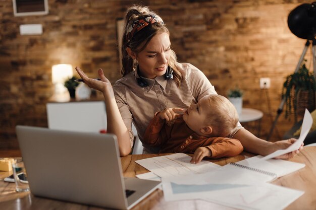 Madre stressata che parla con suo figlio mentre cerca di lavorare a casa