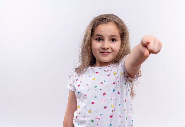 Maglietta bianca da portare sorridente della bambina della scuola che vi mostra gesto su fondo bianco isolato