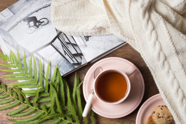 Maglione accogliente; libro; tazza di tè e biscotti con foglie sul tavolo