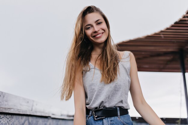 Magnifica giovane donna in cintura nera che ride nel caffè sul tetto. Ritratto all'aperto del modello femminile bianco rilassato con l'acconciatura dritta.