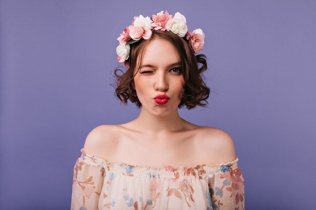 Magnifico modello femminile bianco con fiori nei capelli in piedi. Sensuale ragazza dai capelli corti in posa con l'espressione del viso baciante.