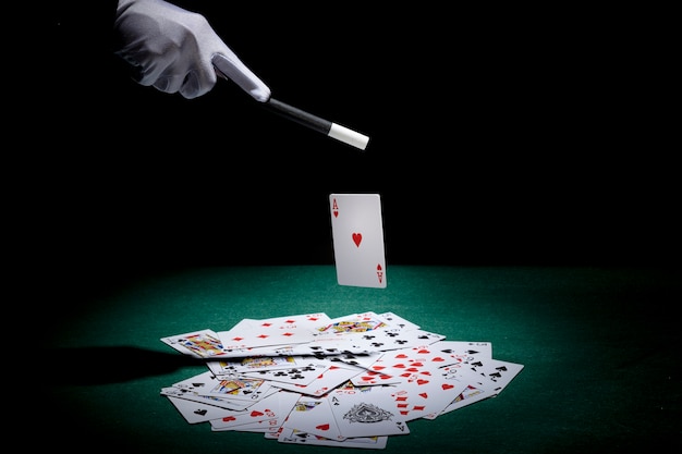 Mago che esegue il trucco su carte da gioco con la bacchetta magica sul tavolo da poker