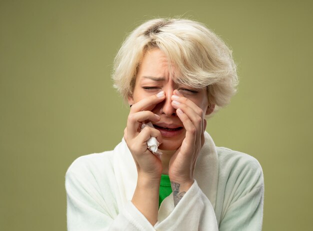 Malata malsana donna con i capelli corti sensazione di malessere che soffre di naso che cola in piedi sopra la parete chiara
