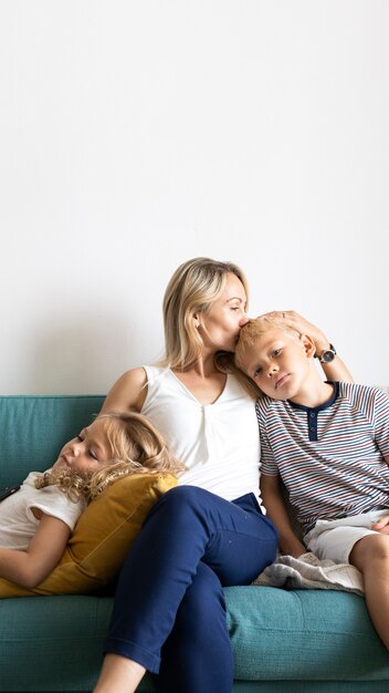 Mamma bionda che bacia la testa di suo figlio e si rilassa con la figlia sullo spazio vuoto del divano