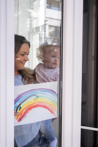 Mamma che tiene bambino e guarda attraverso la finestra