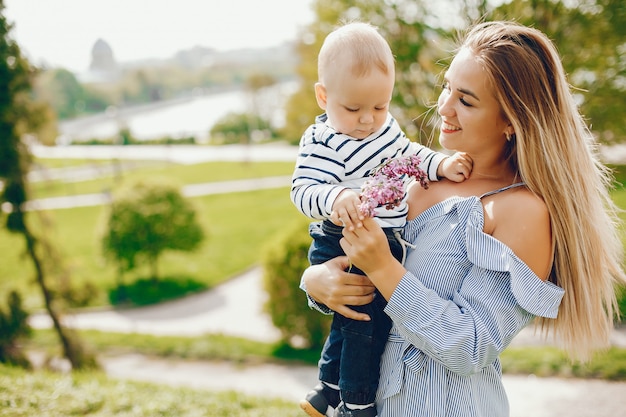 mamma dai capelli lunghi in un abito blu in piedi in un parco solare e tenendo il suo bambino