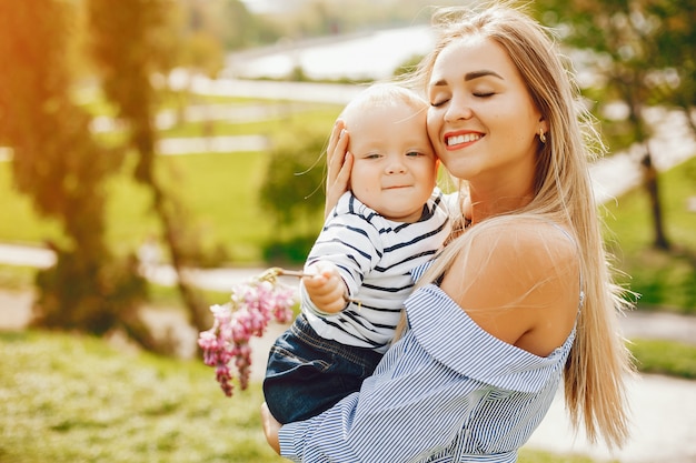 mamma dai capelli lunghi in un abito blu in piedi in un parco solare e tenendo il suo bambino