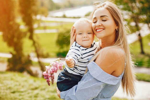 mamma dai capelli lunghi in un abito blu in piedi in un parco solare e tenendo il suo bambino