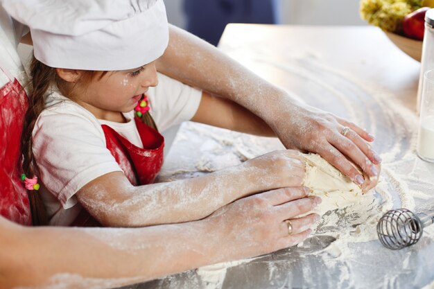 Mamma e figlia con gli stessi vestiti si divertono a preparare un impasto su un&#39;accogliente cucina