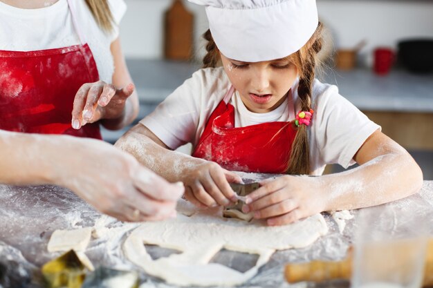 Mamma e figlia con gli stessi vestiti si divertono a preparare un impasto su un&#39;accogliente cucina