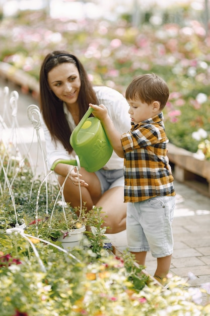 Mamma e figlio con un annaffiatoio verde nella serra. Piccolo bambino che innaffia i fiori in una serra