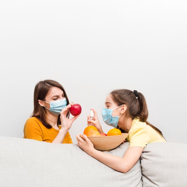 Mamma e ragazza con maschera e frutta a casa