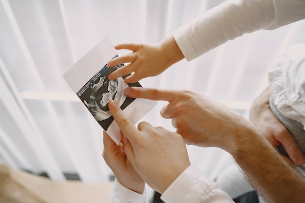 Mamma papà e figlia che guardano la foto ecografica del bambino. Famiglia in abiti leggeri. Famiglia in attesa di un bambino.