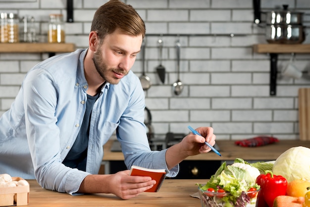 Man scrittura ricetta o dieta vegetale sul suo diario a spirale