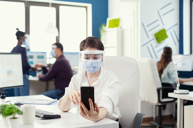 Manager che utilizza lo smartphone per la conferenza online indossando la maschera facciale contro il covid-19 come precauzione di sicurezza