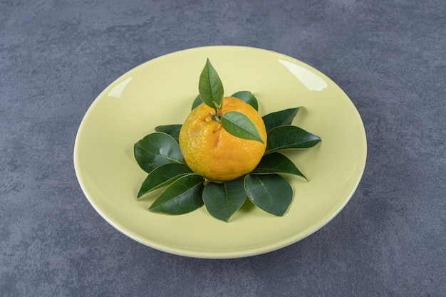 Mandarino biologico fresco con foglie sulla zolla gialla.