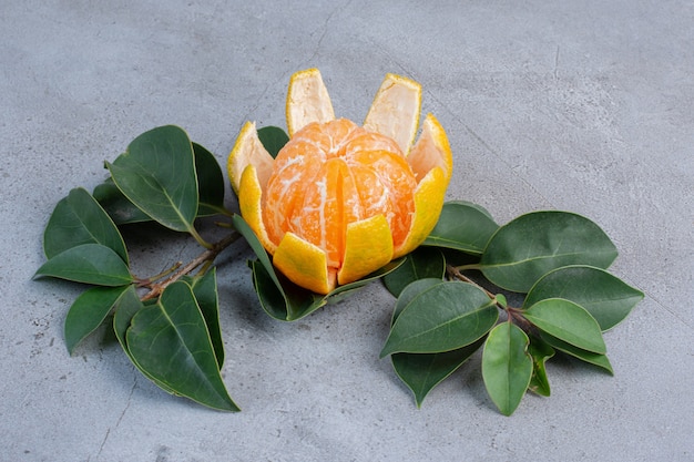 Mandarino sbucciato e foglie decorative su fondo di marmo.