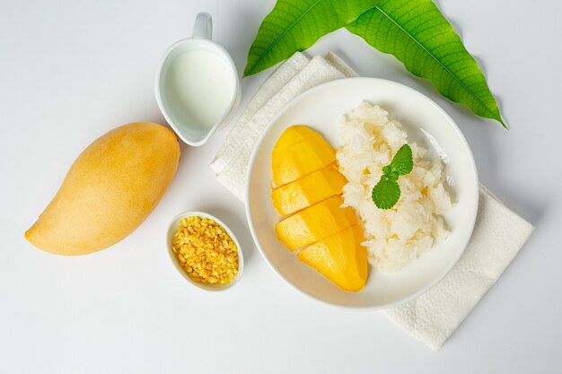 Mango maturo fresco e riso appiccicoso con latte di cocco sulla superficie bianca