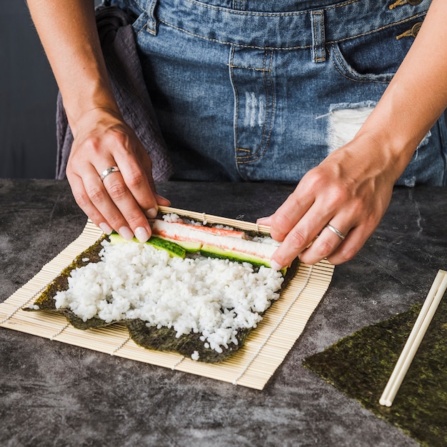 Mani che avvolgono gli ingredienti sulla stuoia di sushi