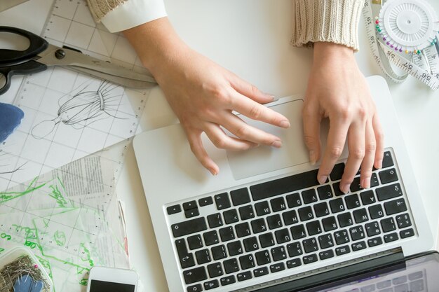 Mani che lavorano con un computer portatile, accessori per cucire in giro