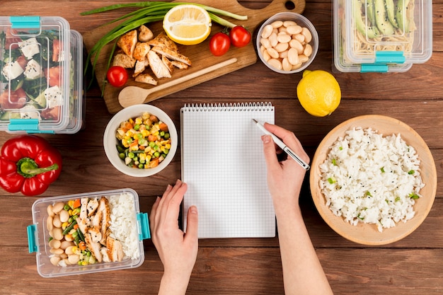 Mani che scrivono sul taccuino con l'alimento dell'annuncio delle casseruole